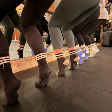 Group practicing ballet or barre exercises wearing colorful grip socks and leggings.