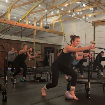 Group fitness class with women exercising using mini trampolines and light weights.