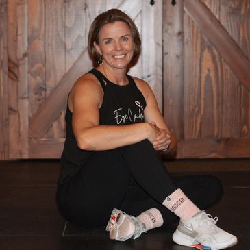Woman in athletic wear sitting on the floor smiling against a wooden background.