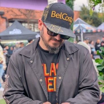 Man wearing a BelCosta cap and sunglasses at an outdoor event.