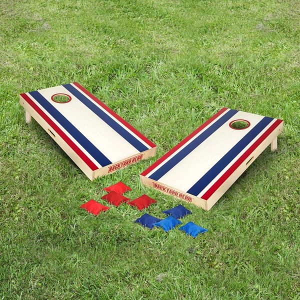 Two wooden cornhole boards with red, white, and blue stripes and bean bags on grass.
