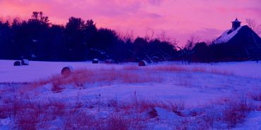 Snow covered hay bales and an old barn in the after glow of a winter sunset