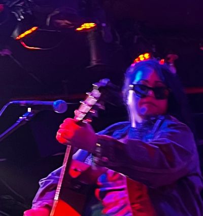 Musician playing guitar on stage under colorful lights.