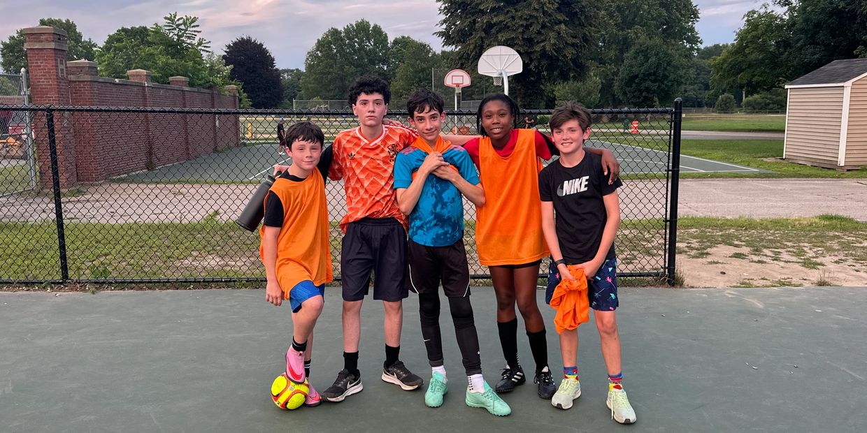Five kids posing on a soccer field.