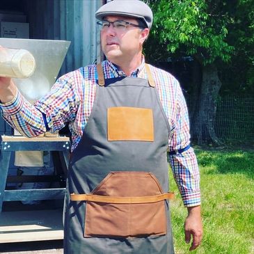 Man in apron and cap holding a container outdoors.