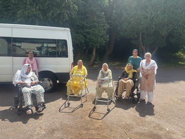 Group of elderly women outdoors with mobility aids and a white van in the background.