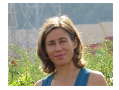 Woman smiling in a natural outdoor setting with greenery.