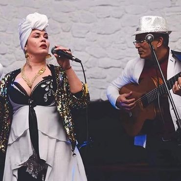 A woman singing and a man playing guitar, both dressed stylishly for a performance.