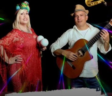 A woman in colorful headwrap with maracas and a man playing guitar.