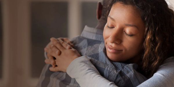 Young woman hugging someone with closed eyes and a smile.
