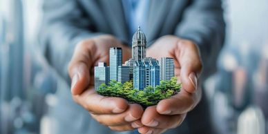 Hands holding a miniature cityscape with buildings and greenery.