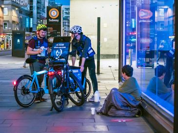 2 volunteers on street cycles serving a rough sleeper
