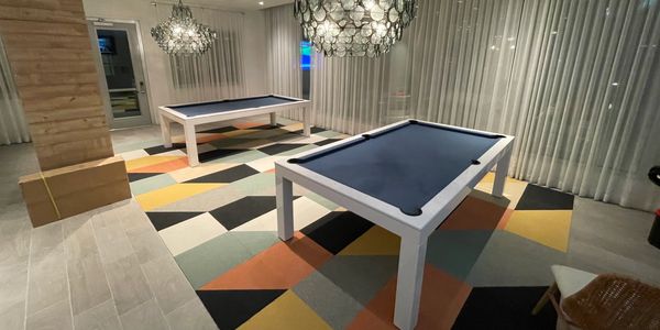 Modern room with two white pool tables and colorful geometric carpet.