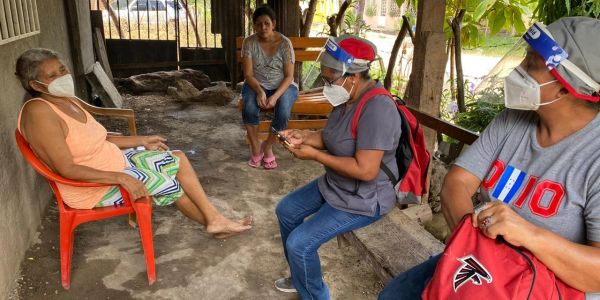 Health workers visiting an elderly woman outdoors.