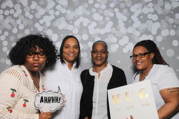 Four women posing with signs at a cheerful event against a bokeh backdrop.