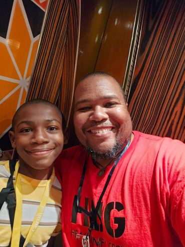 A smiling man and boy take a selfie together indoors with colorful patterned walls.