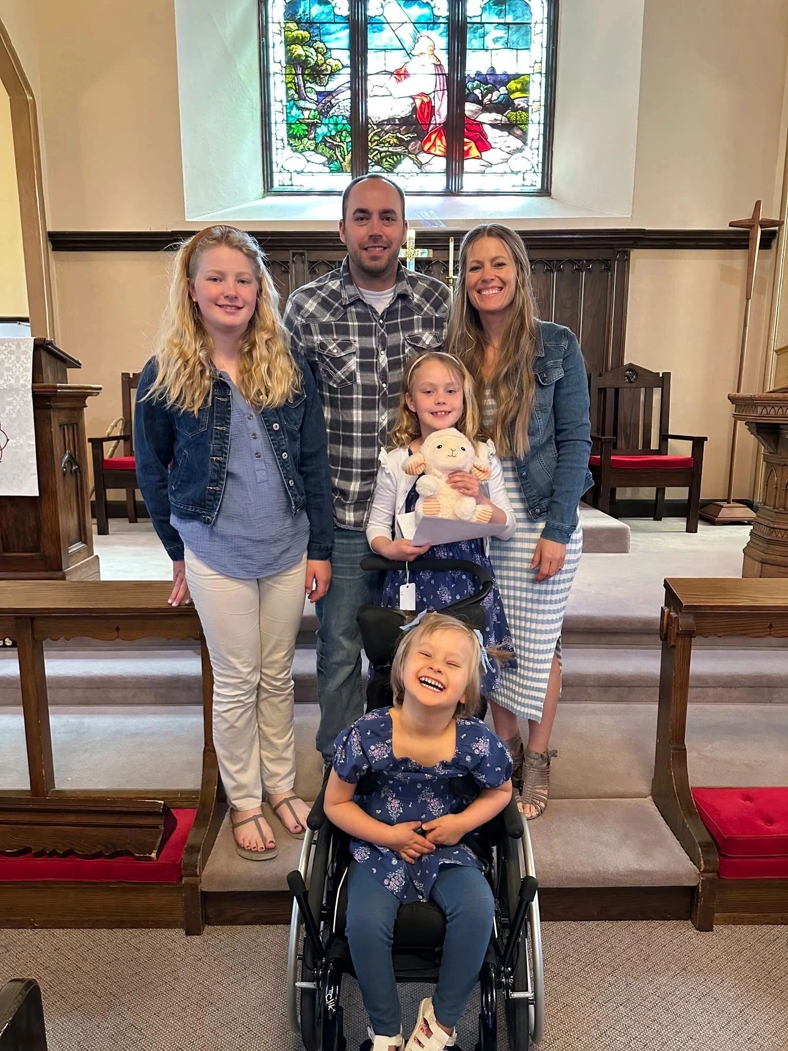 A happy family poses inside a church with a stained glass window behind them.