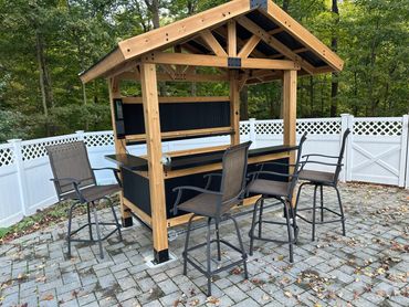 Outdoor wooden bar with four high chairs on a stone patio.