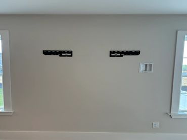 Empty wall with TV mounts between two windows.