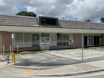 Empty storefront with parking lot under cloudy sky.