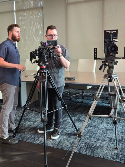 Two men operating professional cameras on tripods indoors.