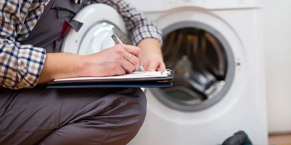 image shows a technician taking notes on a clipboard while inspecting a washing machine