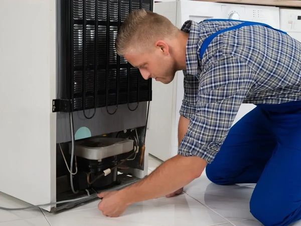 image shows a technician repairing the back of a refrigerator