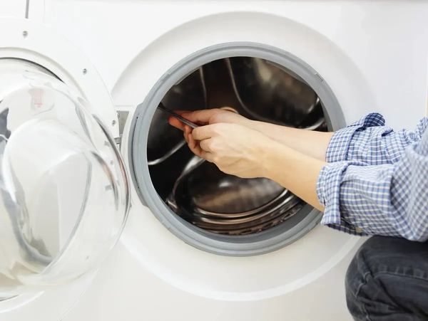 image shows a person repairing a front-loading washing machine