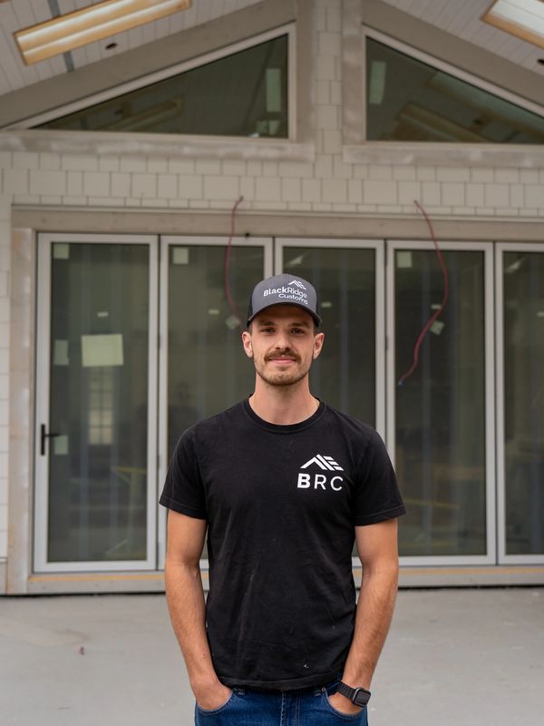 Man in a Black Ridge Customs hat and BRC t-shirt stands in front of a modern building.