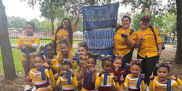 Cheerleading team proudly holding ribbons and a championship banner outdoors.