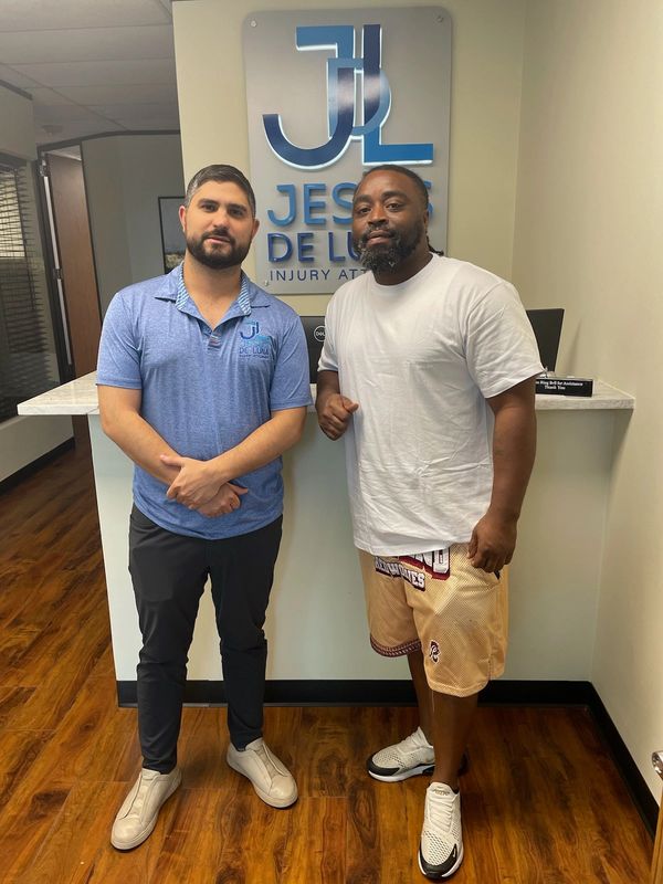 Two men standing inside a law office with a sign behind them.
