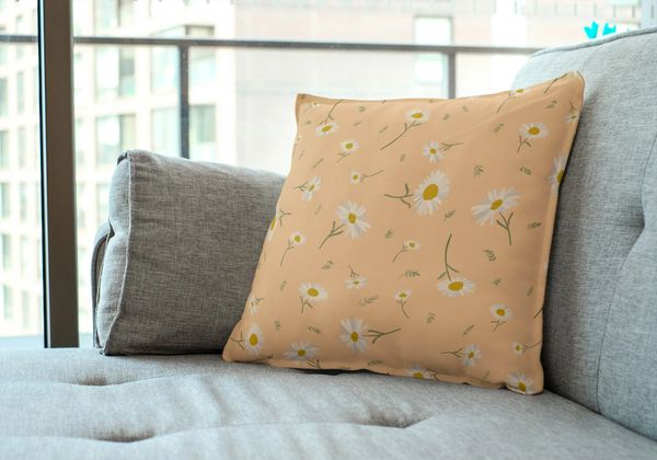 A couch pillow with an illustration of daisies on a peach background.