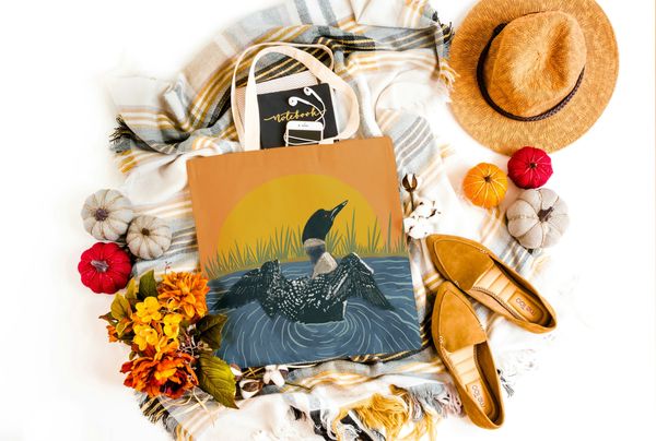Autumn themed mock-up with a tote bag with a colorful loon illustration with a sunset.