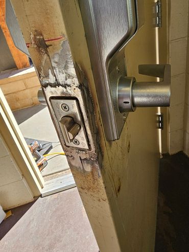 Close-up of a metal door handle and latch on a worn, partly damaged door.
