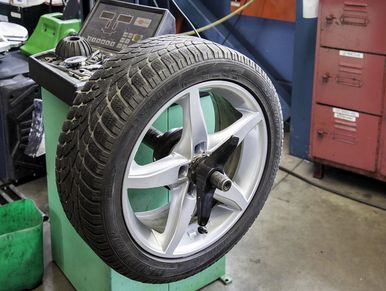 Car wheel mounted on a tire balancing machine in a workshop.