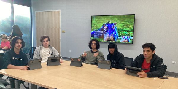 Five young men sitting at a conference table with tablets.