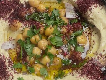 Creamy hummus garnished with chickpeas, parsley, onions, olive oil, and sumac.