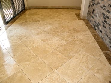 polished travertine with dark brown tile boarder and brick accent wall on right side