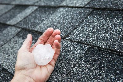Hand holding a large hailstone on a roof.