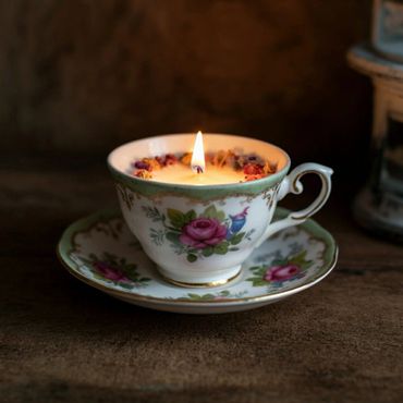 A floral teacup candle with a lit flame on a matching saucer.
