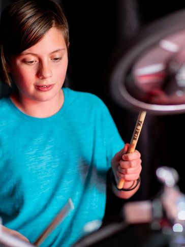 Young person playing drums with focused expression.