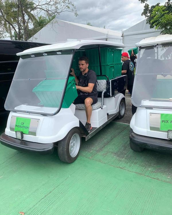 Man loading green crates into a white golf cart labeled 'CP Production'.