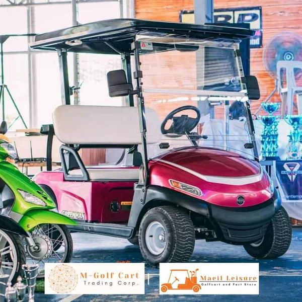 Red golf cart with white seats parked indoors beside a green motorcycle.