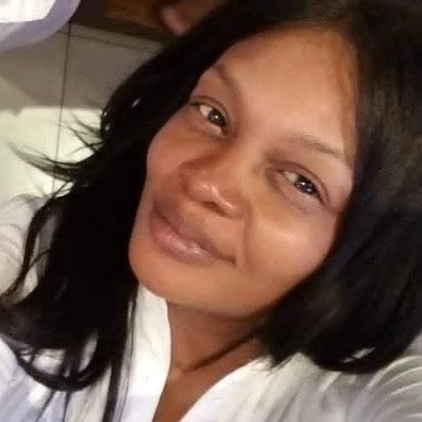Close-up of a woman with long black hair and a white top smiling gently.