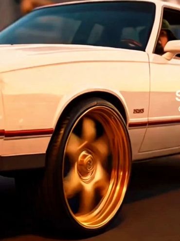 White classic car with shiny gold rims driving at sunset.