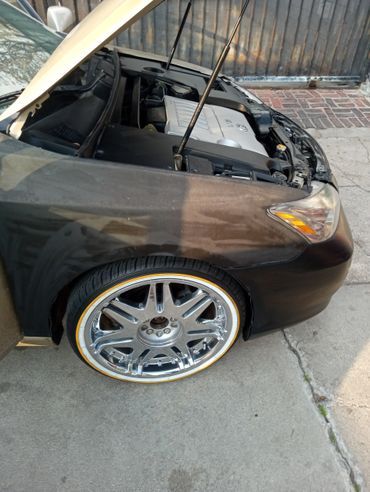 A black car with its hood open and shiny chrome wheels.