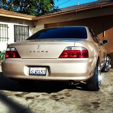 Rear view of a beige Acura sedan with shiny rims parked in a driveway.