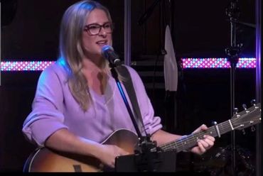 Woman singing and playing guitar on stage with microphone.