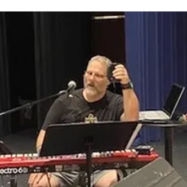 Man playing keyboard and holding a microphone on stage.