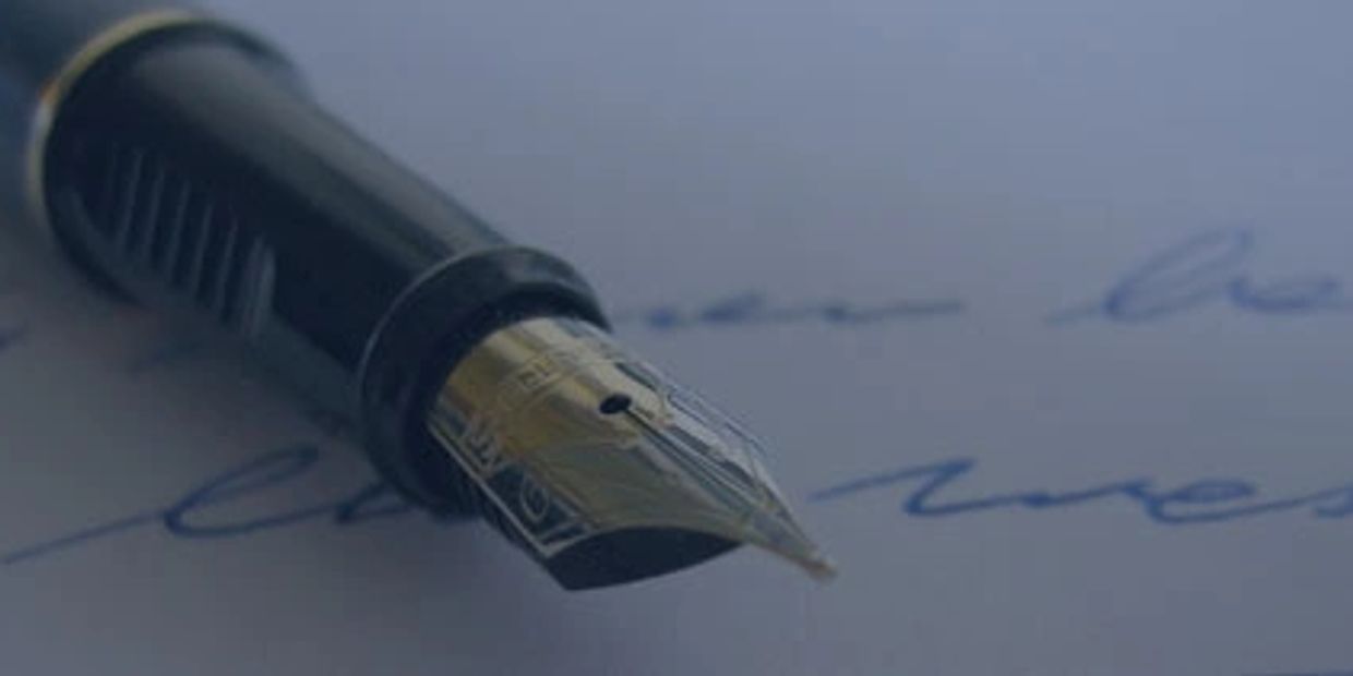Close-up of a fountain pen nib on handwritten blue ink text.
